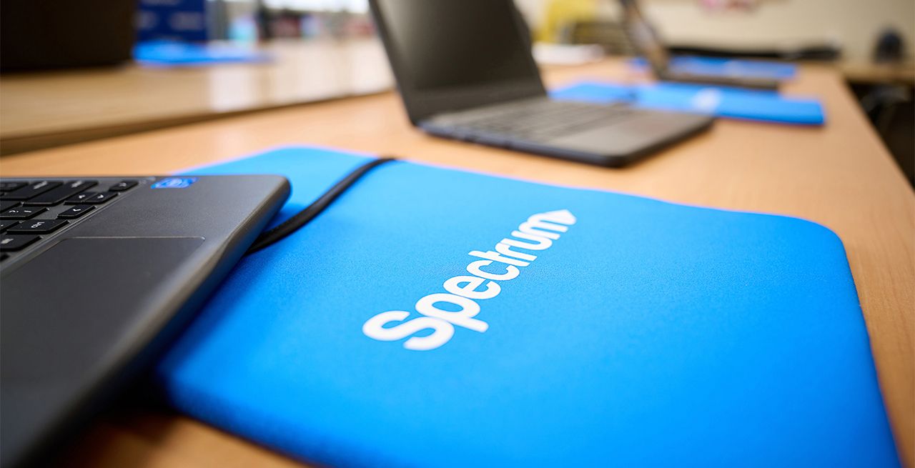 Laptops sitting in an empty computer lab, each with a Spectrum branded mouse pad