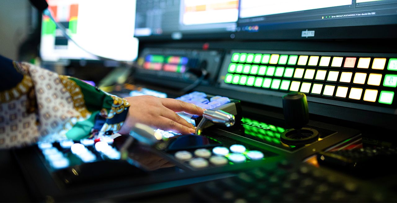 Inside the studio control room at Spectrum Networks, panel of lighted switches and knobs with a hand shown on a lever